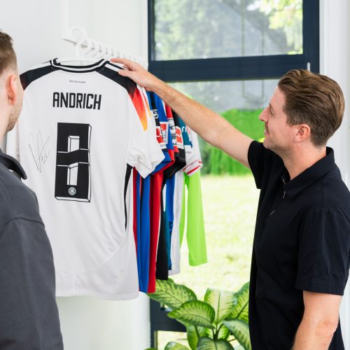 Zwei Maenner betrachten Sporttrikots an Kleiderstaender