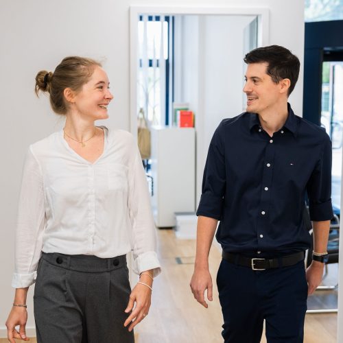 Frau und Mann gehen lachend durch hellen Buero-Flur